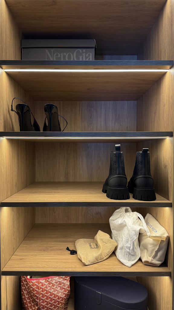 Errores comunes al diseñar un vestidor a medida y cómo evitarlos 1 Vestidor lineal abierto a medida hecho en roble con cajoneras y guías ocultas, barras de colgar a medida con forma de U en color negro, baldas para almacenar zapatos e iluminación integrada